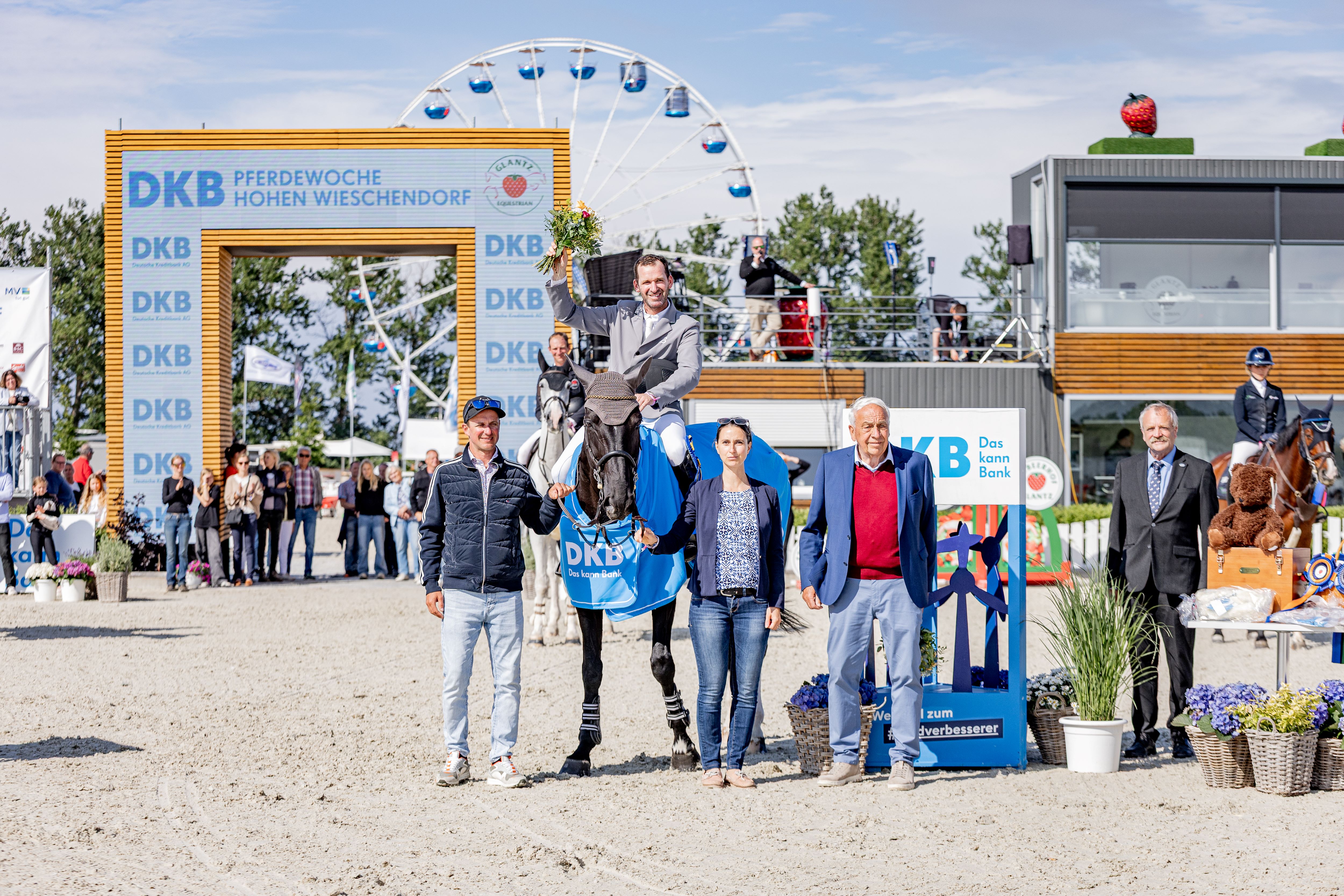Laechelnder Reiter auf schwarzem Pferd mit blauer Decke, Gruppe und Riesenrad