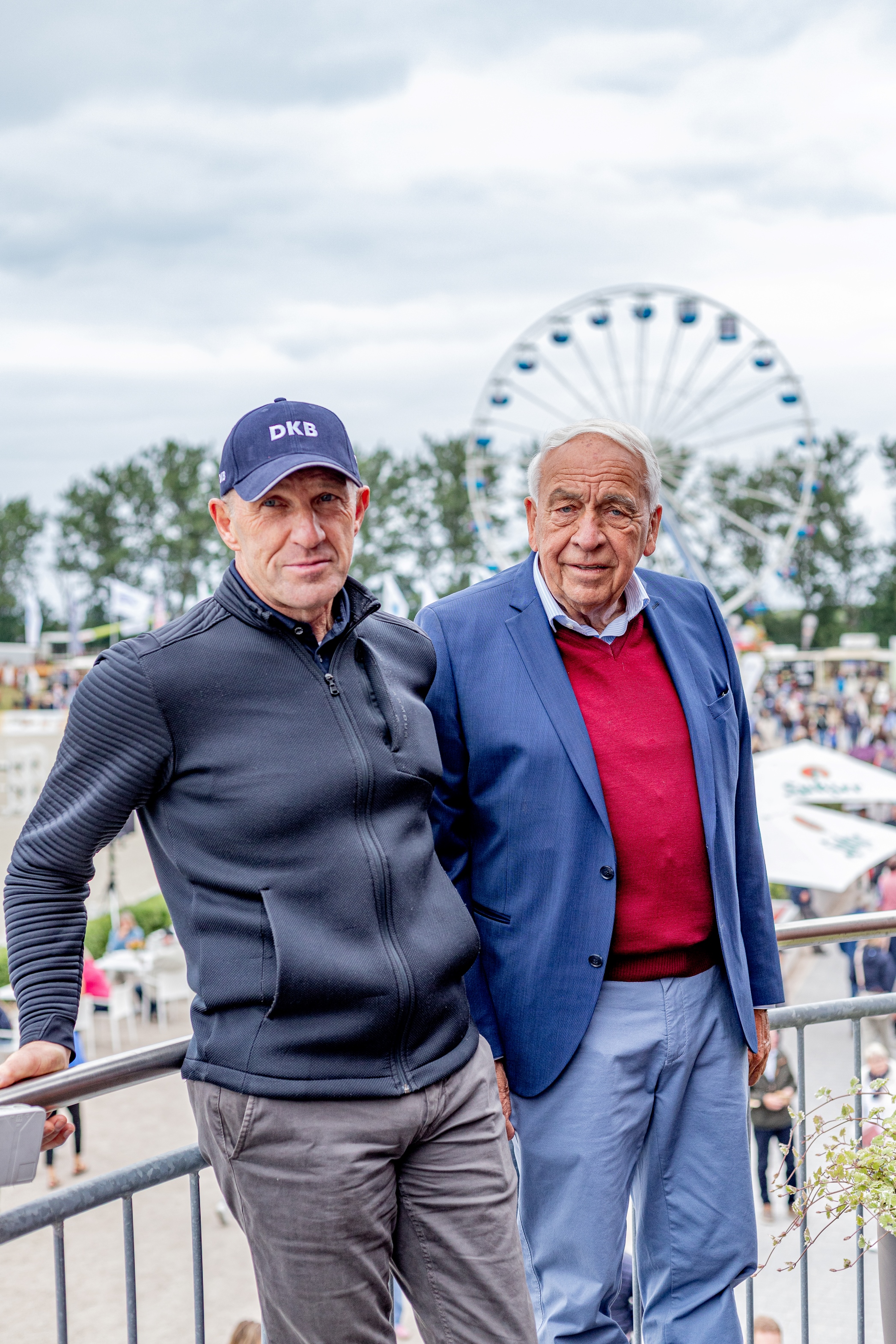 Zwei Maenner, laechelnd, blau und grau, mit Riesenrad im Hintergrund